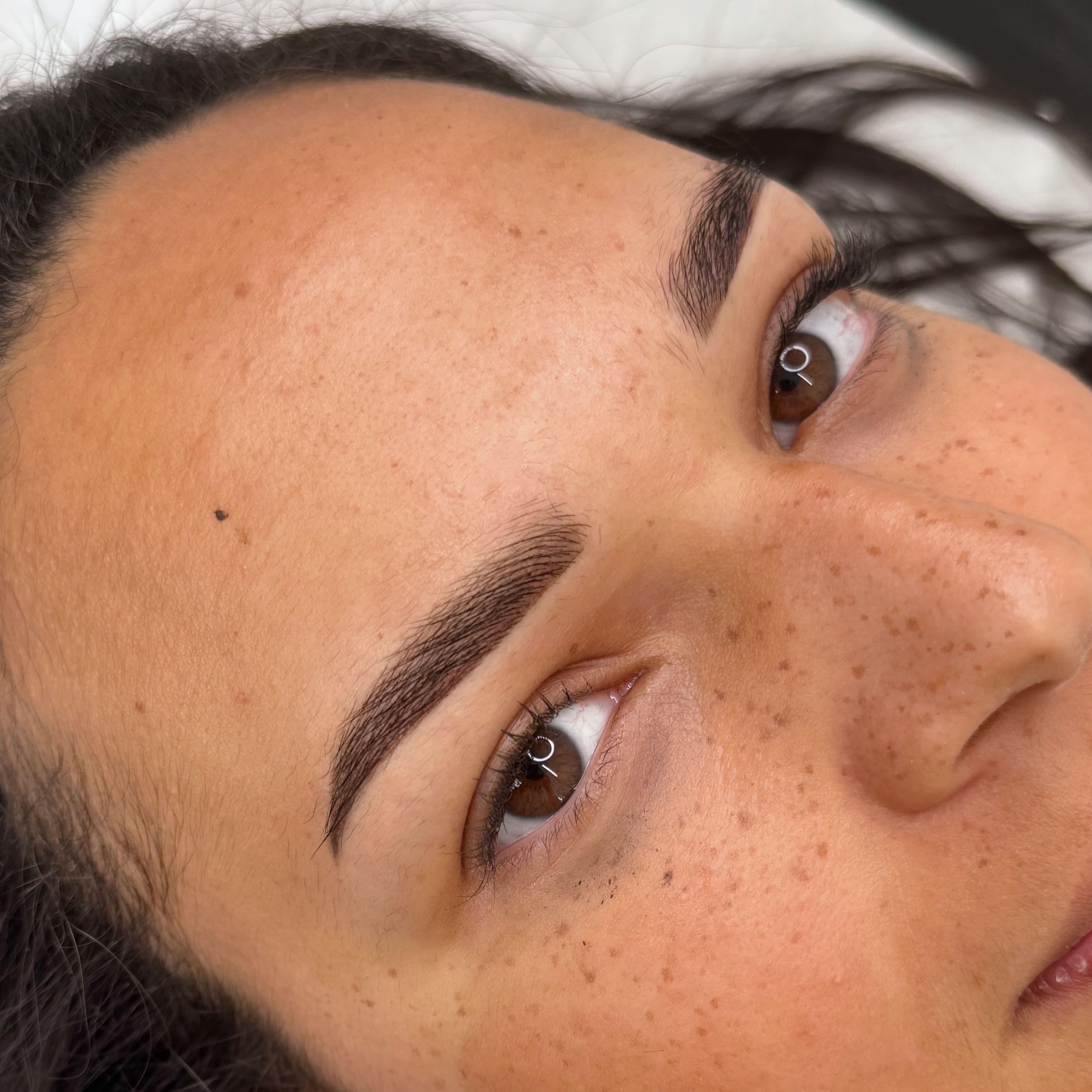 Dermopigmentation permanente des sourcils marron foncé sur peau mate, restructuration intense du regard avec une technique de microshading précis.